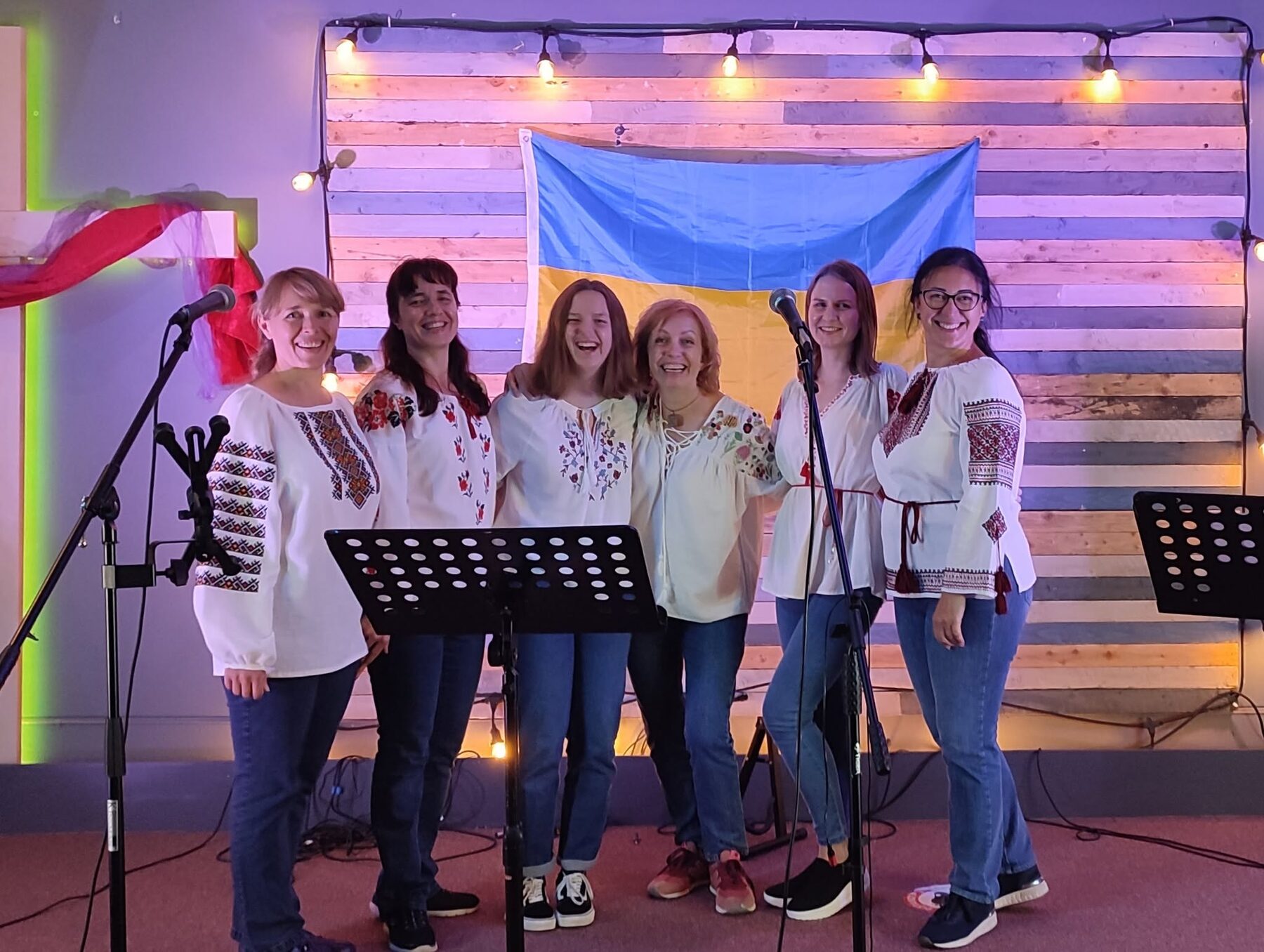 Ukrainian Voices singing on stage in vyshyvanky, before a Ukrainian flag